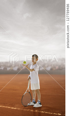 Young tennis player poised to serve on clay court with cloudy sky backdrop. Kids aspirations Young tennis player poised to serve on clay court with cloudy sky backdrop. Kids aspirations 127789486