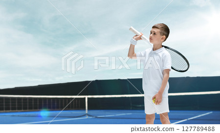 Young boy in tennis outfit holding racket and ball on blue court under clear sky. Visualizing goals Young boy in tennis outfit holding racket and ball on blue court under clear sky. Visualizing goals 127789488