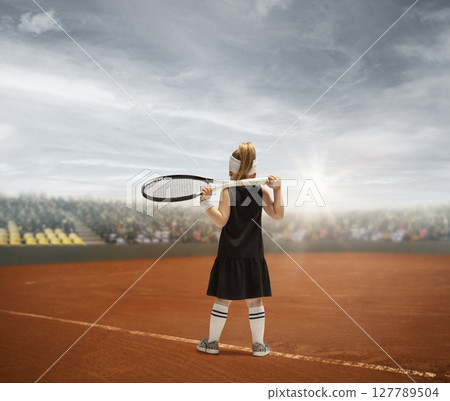 Female tennis player holding racket on clay court with dramatic cloudy sky. Children's dreams 127789504
