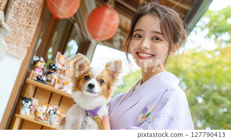 A smiling woman in traditional Japanese clothing and her dog visiting a shrine 127790413
