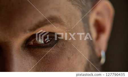 Bold dopamine. Closeup of man's eye with makeup and earring in warm light Bold dopamine. Closeup of man's eye with makeup and earring in warm light 127790435