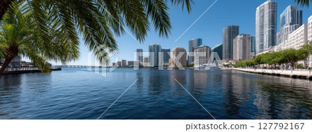 Vibrant skyline reflects in calm waters with swaying palm trees creating a tropical atmosphere on a bright sunny day Vibrant skyline reflects in calm waters with swaying palm trees creating a tropical atmosphere on a bright sunny day 127792167
