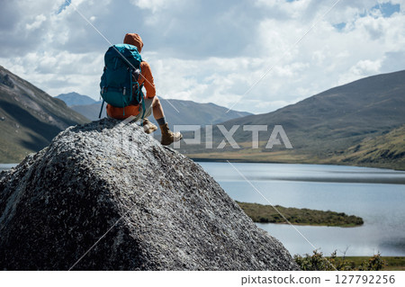 Backpacking woman sit on high altitude mountain top,enjoy the view of a lake in the distance Backpacking woman sit on high altitude mountain top,enjoy the view of a lake in the distance 127792256