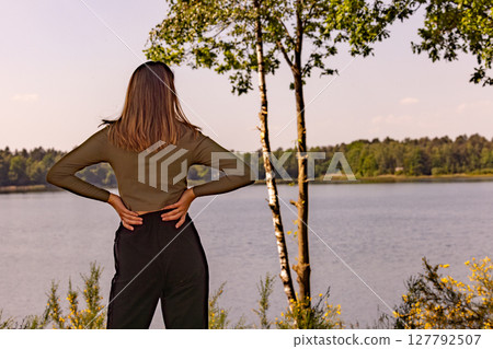 A Thoughtful and Contemplative Woman Sitting by a Serene Lake Surrounded by Natures Beauty 127792507