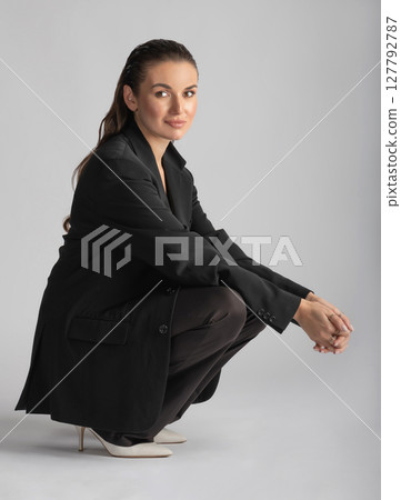 Studio portrait of beautiful woman with black suit and wet hair squatting on floor 127792787