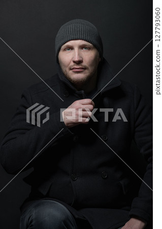 Serious man with black winter coat and winter hat studio portrait 127793060