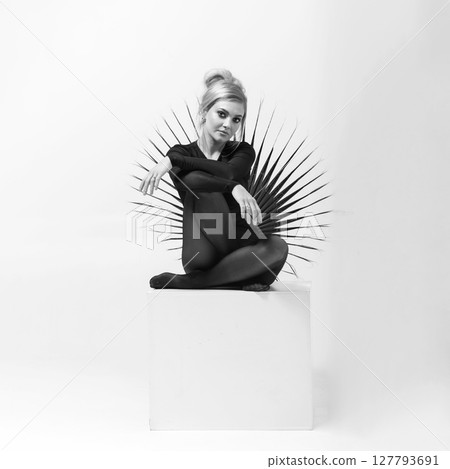 Black and white portrait of beautiful woman with tight black clothes sitting on white cube 127793691
