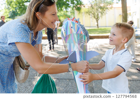 Happy mom giving smiling son boy holds colorful shark-shaped Schultuete filled with gifts his first day school Germany. Shiny cone with fins eyes symbolizes tradition excitement for new beginnings Happy mom giving smiling son boy holds colorful shark-shaped Schultuete filled with gifts his first day school Germany. Shiny cone with fins eyes symbolizes tradition excitement for new beginnings 127794568