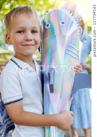 Smiling boy holds colorful shark-shaped Schultuete filled with gifts on his first day of school in Germany. Shiny cone with fins and eyes symbolizes tradition and excitement for new beginnings Smiling boy holds colorful shark-shaped Schultuete filled with gifts on his first day of school in Germany. Shiny cone with fins and eyes symbolizes tradition and excitement for new beginnings 127794583