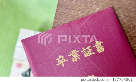 A red-covered diploma placed on a table while cleaning up 127794801