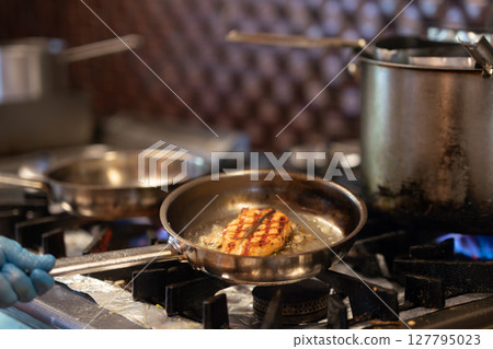 Chef is frying fish in cooking pan. 127795023