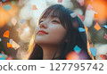 Young Asian woman looks up with a serene expression amidst falling confetti in warm dreamlike lighting. Ideal for themes of joy, celebration and hope 127795742