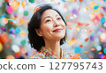 Happy mature Asian woman looks up with joyful smile as colorful confetti falls around her. Ideal for themes of celebration, success and positive emotions 127795743