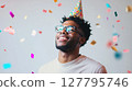 Joyous African American man in a party hat and glasses smiles upwards as confetti falls around him. Perfect for themes of celebration, birthdays and happiness 127795746