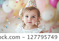 Charming toddler girl in party hat and white dress looks directly at the camera surrounded by soft bokeh and falling confetti. Ideal for themes of birthdays, childhood and innocence 127795749