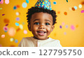 Cheerful African American toddler in colorful party hat smiles broadly, surrounded by falling confetti against yellow background. Perfect for themes of birthdays, childhood joy and innocence 127795750