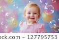 Joyous baby girl with blue eyes smiles widely surrounded by iridescent soap bubbles against soft colorful background. Perfect for themes of infancy, happiness and innocence 127795753