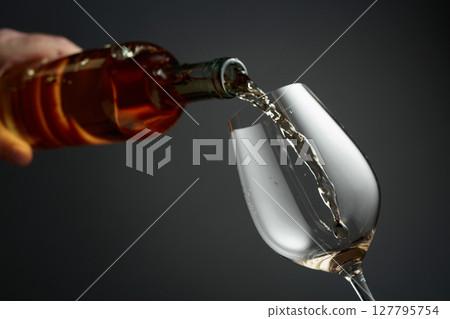 Pouring white wine from a bottle into a glass. 127795754