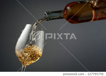 Pouring white wine from a bottle into a glass. 127795756