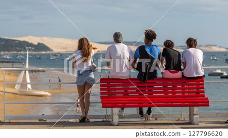 people sitting on a bench looking at the sea 127796620