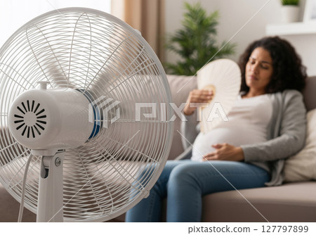Expectant Mother Cooling Down with Electric Fan During Hot Summer Day at Home 127797899