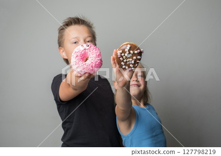 Attractive sister and brother having fun holding donuts standing against white background wall.  127798219