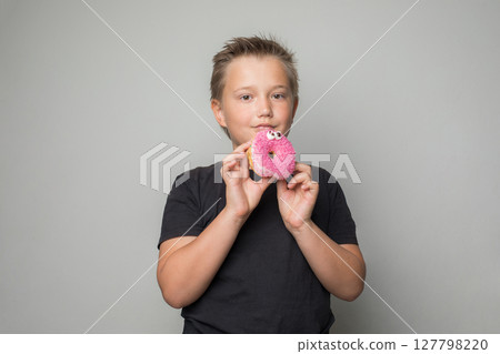 Cute child boy holding testy donut. Kid in black t-shirt with sweet food indoor 127798220