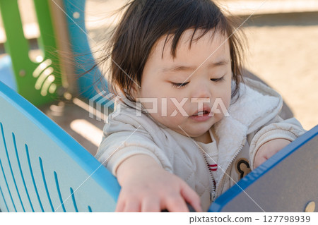 [A one-year-old child playing on the slide in the children's playground at Sagamihara City Asamizo Park] 127798939