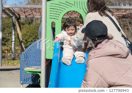 [A one-year-old child playing with his mother and grandmother in the children's playground at Sagamihara City Asamizo Park] 127798943
