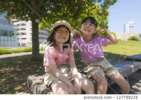 Smiling sisters enjoying summer time on a park bench Smiling sisters enjoying summer time on a park bench 127799228