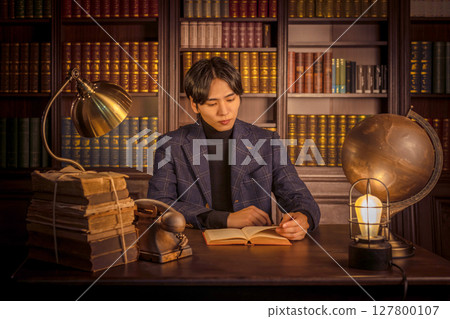 A man reading a book in a room with a bookshelf 127800107
