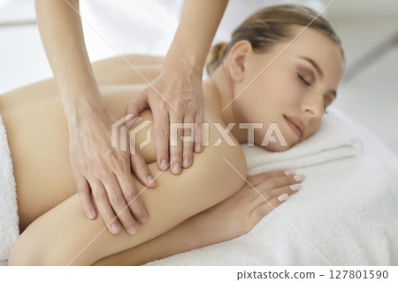 Massage therapist doing relaxing back, neck and shoulders massage treatment for woman 127801590