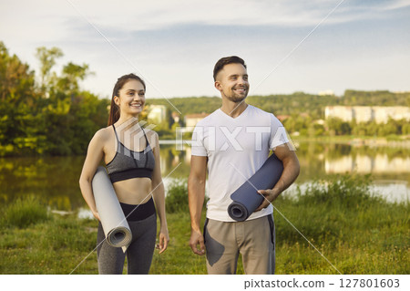 Happy smiling fit couple, sporty people standing looking outdoors with rolled yoga mats, preparing Happy smiling fit couple, sporty people standing looking outdoors with rolled yoga mats, preparing 127801603