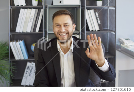 Businessman waving hello, interacting on video call with friendly gesture and open smile, attention 127801610
