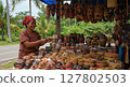 Indonesian Woman Selling Traditional Handcrafted Masks and Woven Baskets at Outdoor Market 127802503