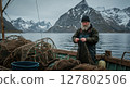Nordic Fisherman Mending Nets on a Boat with Snowy Mountain Backdrop in Norway 127802506