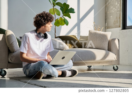 Handsome young male typing on laptop sitting on floor at home Handsome young male typing on laptop sitting on floor at home 127802805