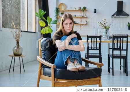 Portrait of young beautiful serious woman looking at camera sitting at home in chair 127802848