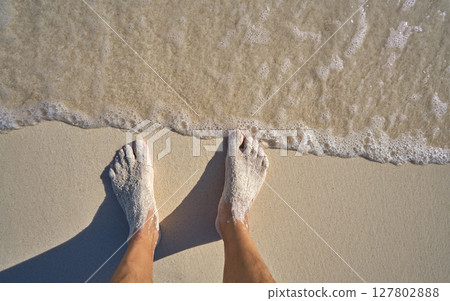 Caribbean tourist male feet on white sand shore 127802888
