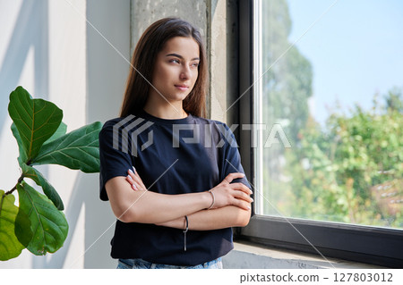 Portrait of confident successful teenage girl posing with crossed arms near window 127803012