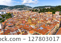 Aerial panorama of the historic Old Town of Nice, France, with vibrant rooftops and green hills in the background on a sunny day. 127803017