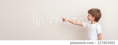 Preschool student wearing a white t shirt, pointing with an index finger at an unseen object on a white background, embodying the excitement of back to school learning and discovery 127803081