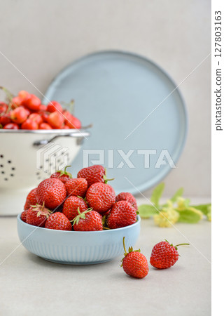 Ripe strawberries in a blue bowl and a white enamel colander full of sweet cherries Ripe strawberries in a blue bowl and a white enamel colander full of sweet cherries 127803163