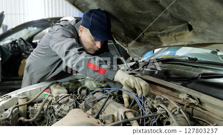 Skilled automotive technician wearing protective gloves, inspecting engine components and diagnosing mechanical problems in well equipped repair workshop 127803237