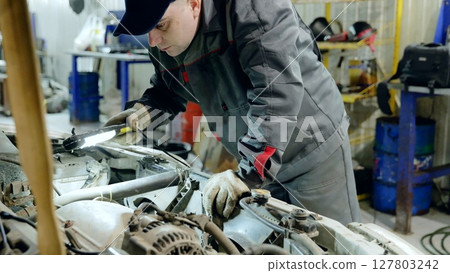 Skilled mechanic checking car engine with flashlight, wearing protective gloves during diagnostic evaluation in professional automotive workshop Skilled mechanic checking car engine with flashlight, wearing protective gloves during diagnostic evaluation in professional automotive workshop 127803242