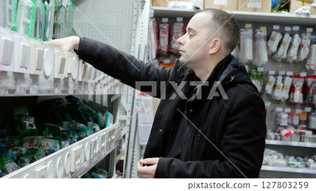 Electrician selecting light switches in a hardware store, reaching for a specific model on a shelf filled with various electrical components 127803259