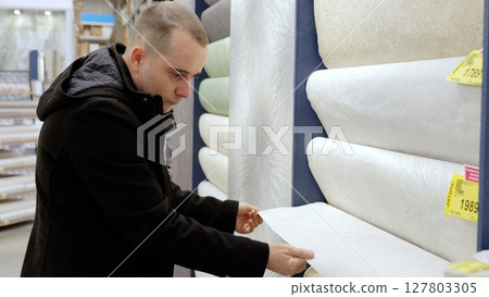 Customer selecting wallpaper samples, comparing patterns and textures while planning home interior design renovation in hardware store showroom Customer selecting wallpaper samples, comparing patterns and textures while planning home interior design renovation in hardware store showroom 127803305