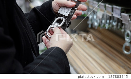 Focused worker gripping metallic carabiner, inspecting hardware details among shelves of professional tools and climbing gear 127803345