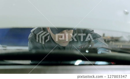 Professional mechanic fixing car windshield with specialized tools in auto service workshop, wearing uniform and protective gear Professional mechanic fixing car windshield with specialized tools in auto service workshop, wearing uniform and protective gear 127803347