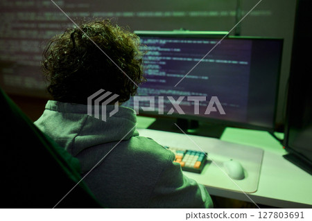 A young programmer codes intently in a dark setting, immersed in his work and creativity 127803691